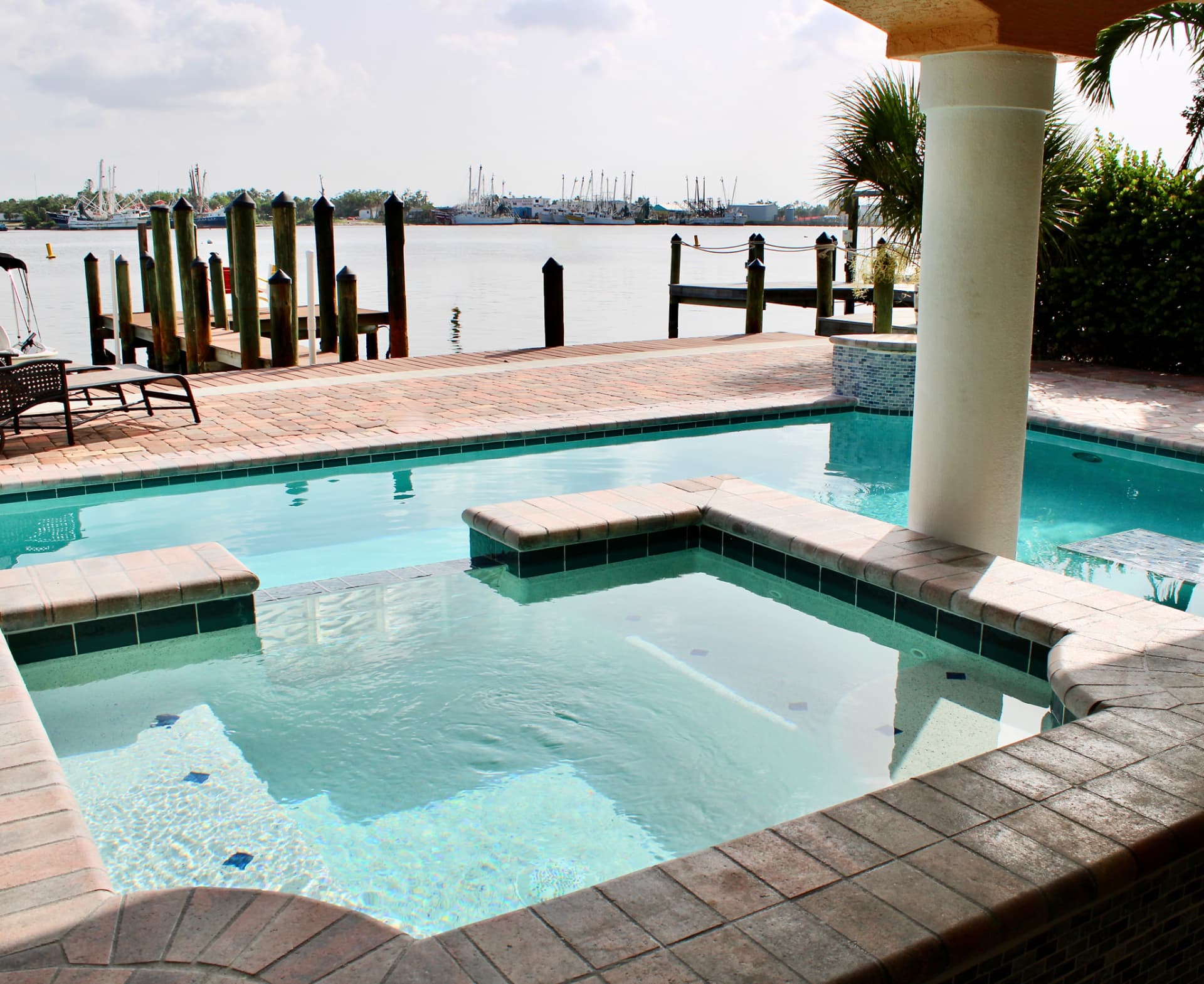 Waterfront pool and spa with paver decking overlooking a dock and harbor