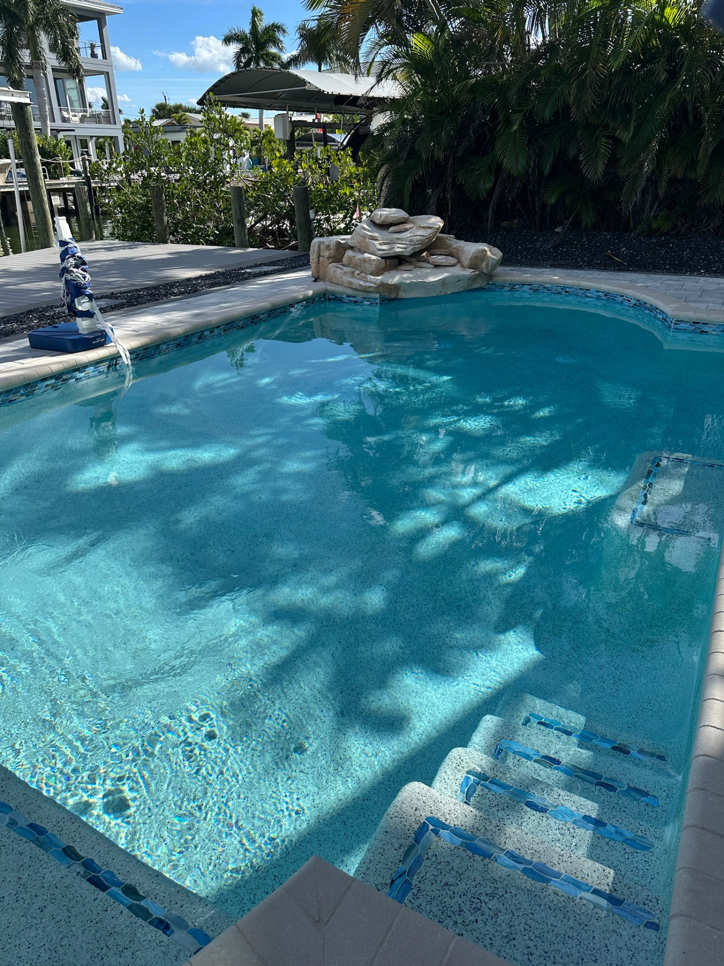 Canal-front pool with tiled entry steps, rock water feature and paver deck