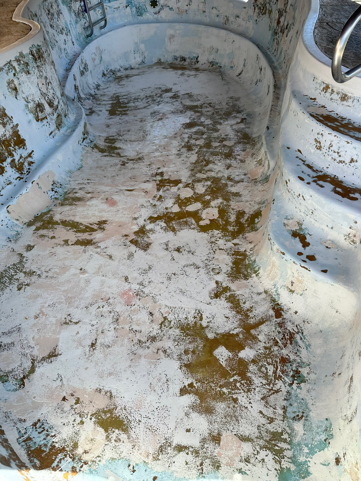 Drained fiberglass pool shell with heavy algae staining and a chalky, failing surface