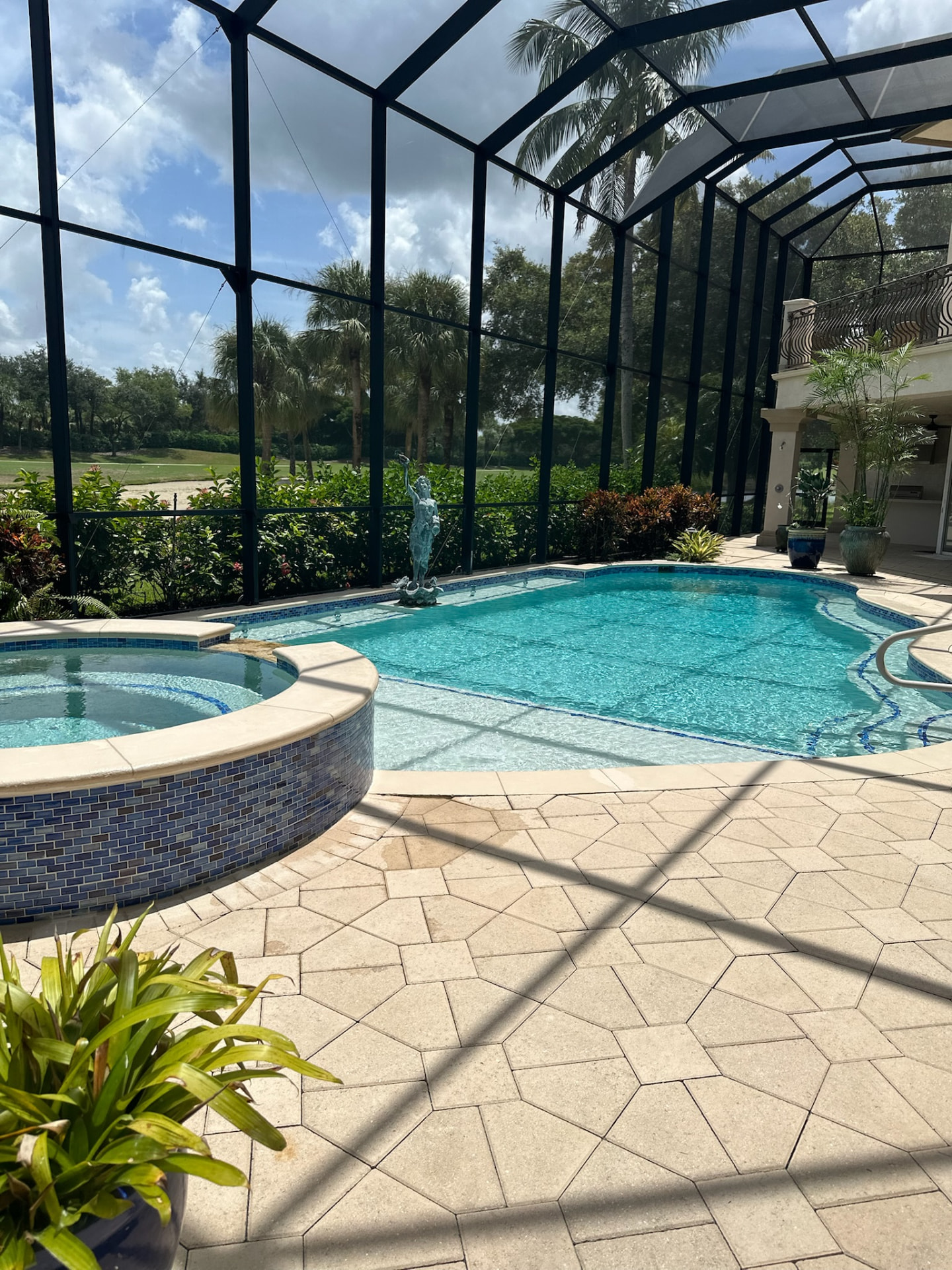 Screened pool with a raised round spa, blue mosaic tile and travertine paver decking